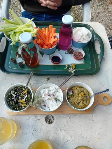 Plateau de légumes crus avec trempettes, boissons et décorations florales sur une table.